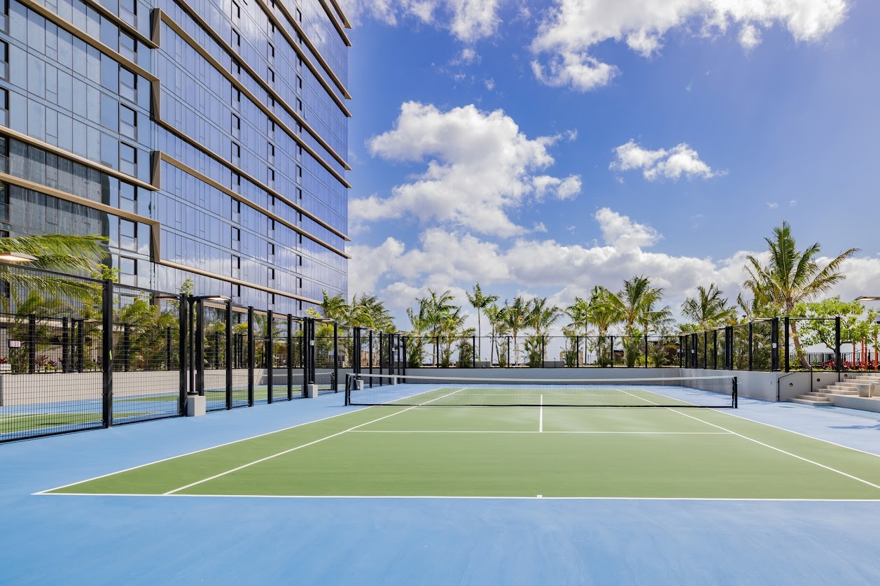 A tennis court is surrounded by a fence and palm trees.